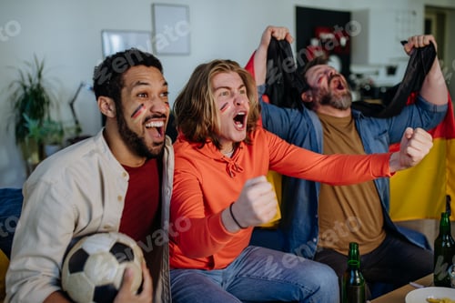 Preview: Happy German football fans friends watching football at home and celebrating