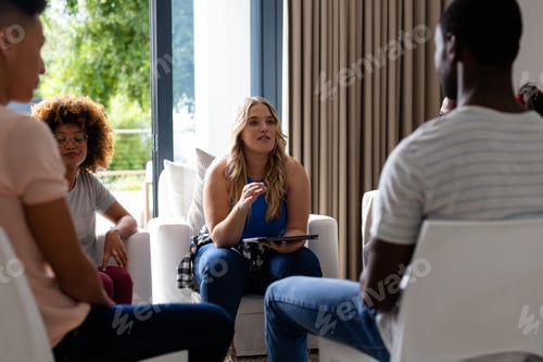 Preview: Happy diverse group of friends using tablet and talking in group therapy session
