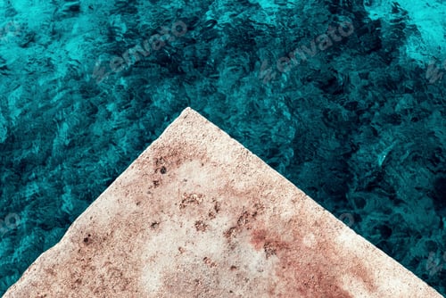 Preview: Overhead shot of a deep blue sea and the brown triangle-shaped stone in the middle