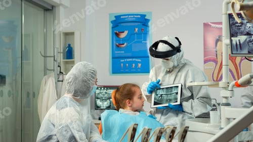 Preview: Dentist in protective equipment showing on tablet dental x-ray of child