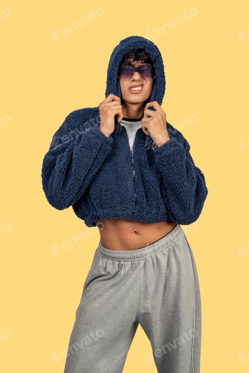 Preview: Young man wearing sunglasses and a blue fluffy cropped hoodie is posing on yellow background