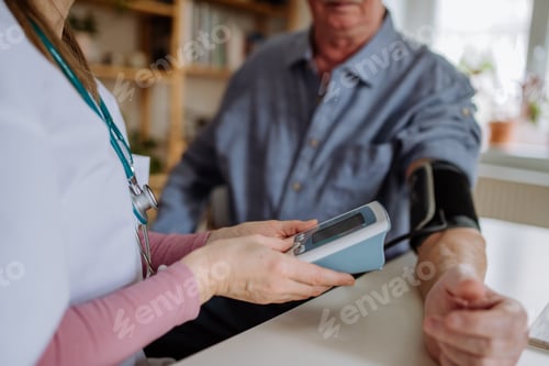 Preview: Female doctor visiting senior man and examinig him indoors at home, measuring blood pressure.