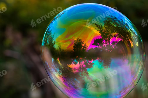 Preview: Close-up of a colorful soap bubble reflecting a vibrant sunset with trees in the background