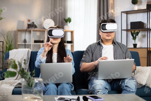 Preview: Asian couple sitting on couch with VR headset and laptop