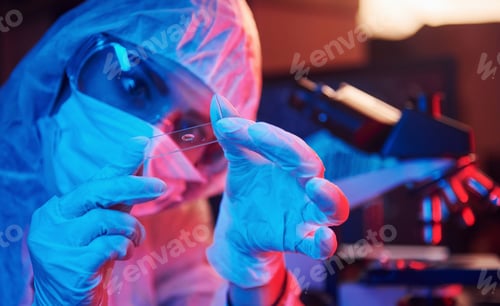 Preview: Nurse in mask and white uniform, holding tube with liquid and sitting in neon lighted laboratory