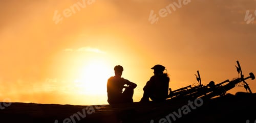 Preview: Silhouette of a couple watching the sunset with their bicycles beside them at the beach