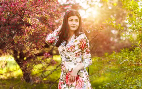 Preview: Graceful woman with charming smile in garden among flowering tree