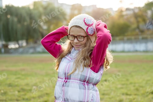 Preview: Portrait of a happy girl 7 years old, in a knitted hat, glasses, autumn sunny background