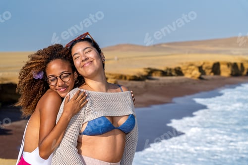 Preview: Two smiling friends embracing on a sunny beach during adventure trip