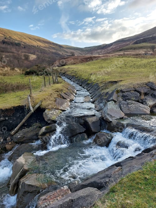 Preview: two streams in manmade stream bed of rocks meeting in welsh landscape