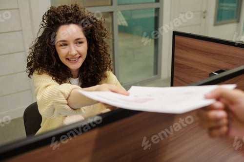Preview: Young smiling female receptionist passing document or application form to client