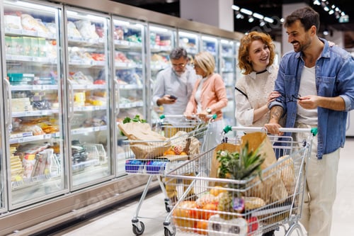 Preview: Happy couple pushing shopping cart in supermarket, choosing frozen food