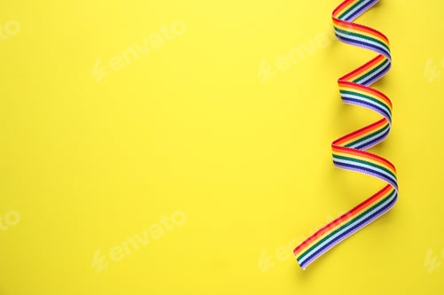 Preview: Top view of rainbow ribbon on yellow background, space for text. Gay symbol