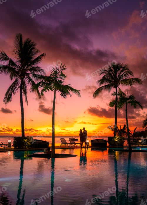 Preview: couple men and woman watching sunset on a tropical beach in Mauritius with palm trees by the