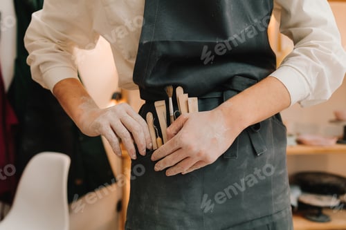 Preview: Various potters tools for clay work. Black apron artisan holds full set of instruments