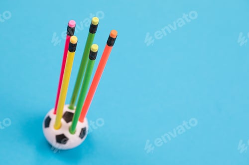 Preview: A round soccer ball shape pencil cup with five colorful pencils in it on azure surface isolated