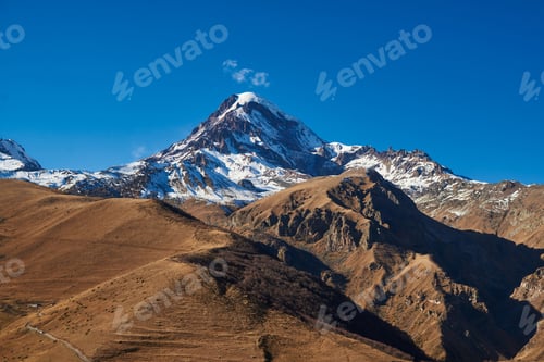 Preview: beautiful natural landscape. a high mountain with a snow cap on top and a small cloud near it in a