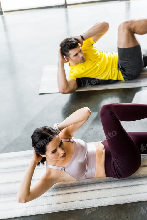 Preview: sportsman and sportswoman doing crunches on fitness mats in sports center