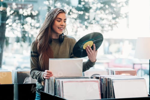 Preview: Woman holding vinyl while choosing record in a music shop.