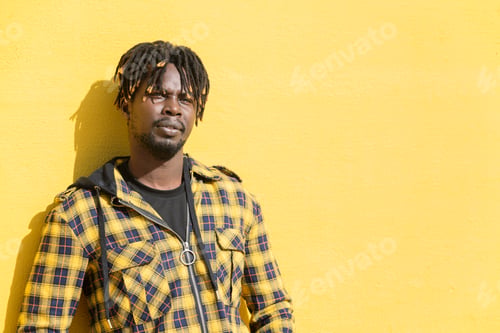 Preview: african man leaning against an intense yellow wall