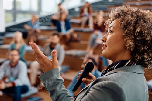 Preview: Mid adult businesswoman giving a speech to group of people during a seminar in conference hall.