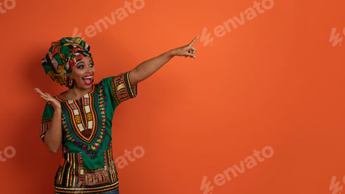 Preview: Emotional black lady in african costume pointing at copy space