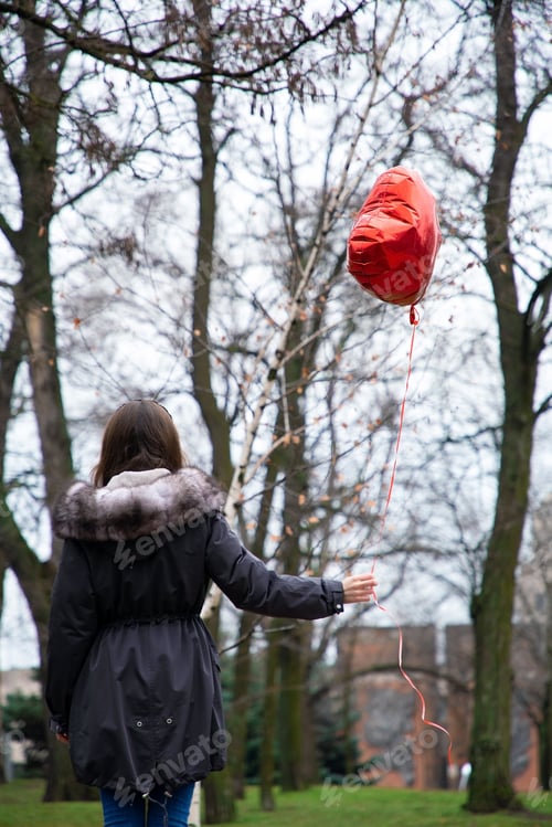 Preview: young woman walking in the park with a heart-shaped balloon