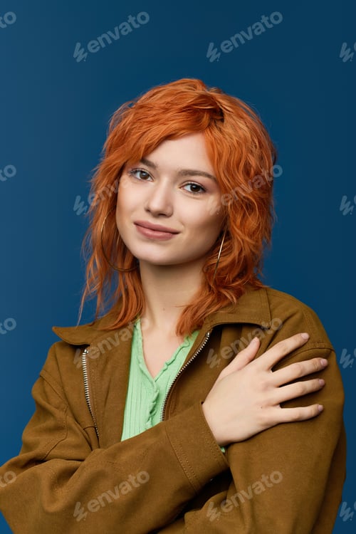 Preview: Young woman displays spring fashion with vibrant red hair against blue backdrop