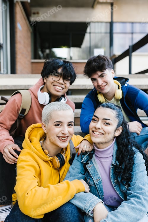 Preview: Vertical shot of multiracial young students sitting at school building entrance
