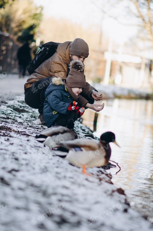 Preview: Man and Child Feeding Ducks on Snowy Bank