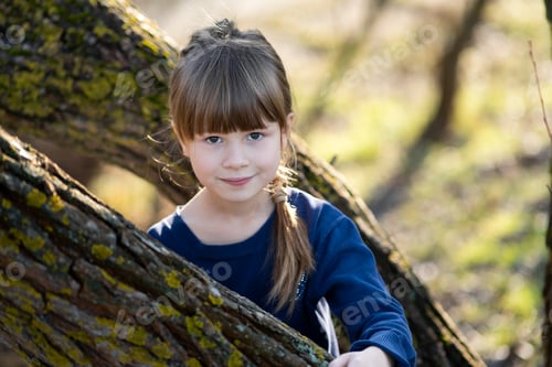 Preview: Portrait of a pretty child girl standing near a tree trunk in autumn outdoors
