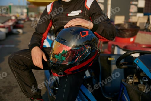 Preview: Crop view of kart racer sits confidently on his gokart and holding a helmet