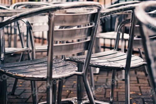 Preview: Empty outdoor restaurant metallic patio chairs wet from the rain.