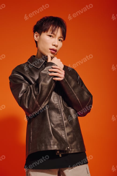 Preview: Stylish young man posing confidently against a vibrant orange backdrop in modern urban fashion
