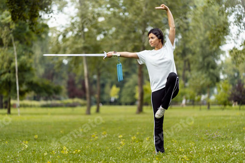 Preview: Martial arts woman practicing wushu kungfu with sword at green park