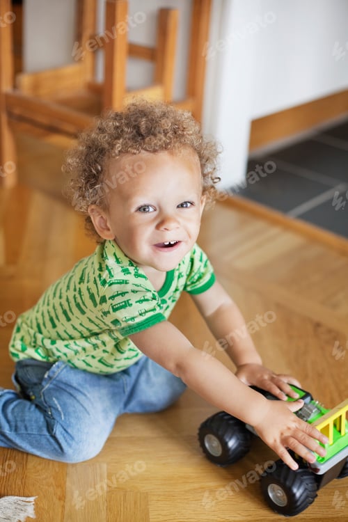 Preview: Portrait of cute boy playing with toy car on hardwood floor at home