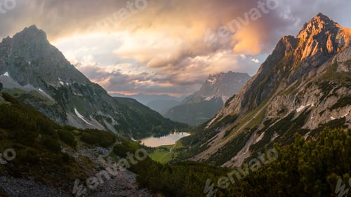 Preview: Beautiful scenery of huge rocky mountains surrounding a lake in cloudy sky background at sunset