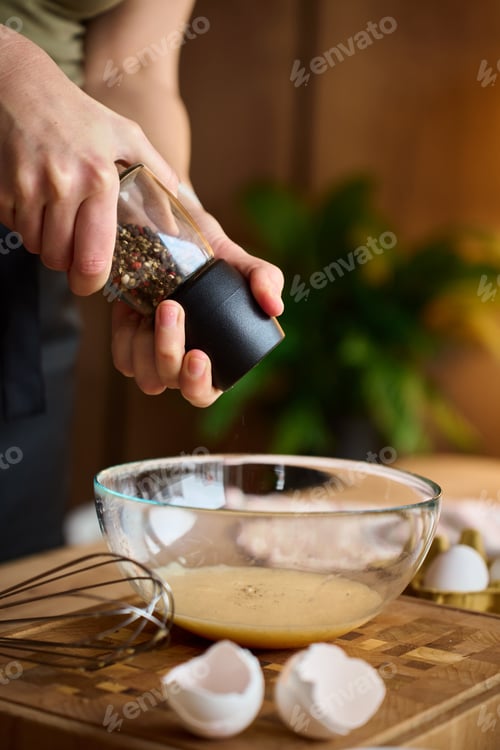 Preview: Hands grinding pepper into egg mixture in glass bowl on kitchen counter