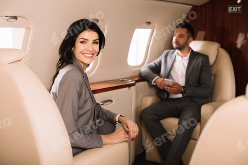 Preview: selective focus of cheerful businesswoman in private jet with businessman