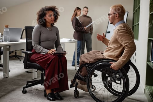 Preview: Caucasian Man with Disability Discussing Project with Black Woman in Office