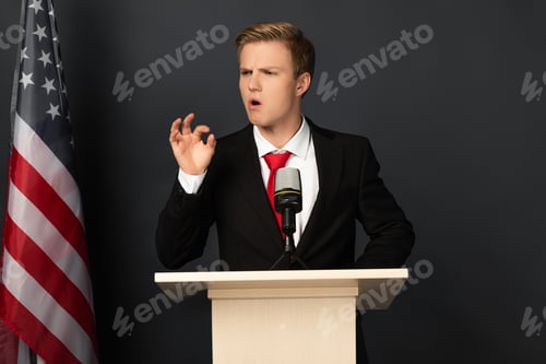 Preview: emotional man gesturing on tribune with american flag on black background