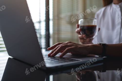 Preview: Closeup image of a business woman working on laptop computer while drinking coffee in office