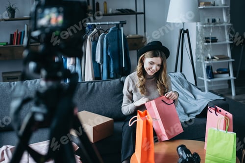 Preview: smiling fashion blogger looking into shopping bags and recording new video for vlog