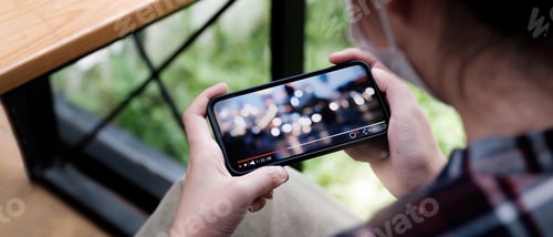 Preview: Cropped image of female hand holding smartphone and watching video while standing outdoor.
