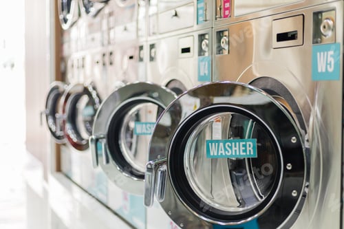 Preview: Two washers are in focus at a laundromat located in a busy area.