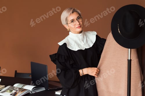 Preview: young woman fashion stylist wearing black white dress touching clothes in modern work place