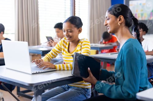 Preview: In school, Indian female teacher helping student using laptop in classroom, smiling together