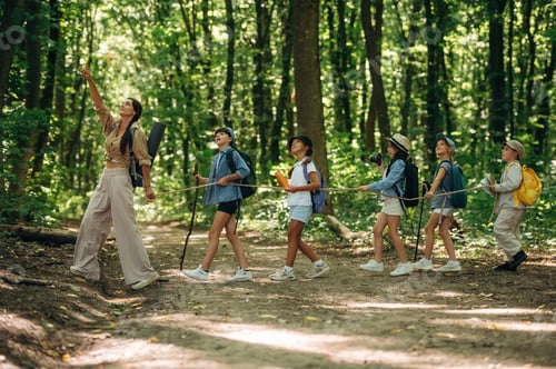Preview: Hand gesture, showing something, pointing at. Woman is doing tour for group of kids in the forest