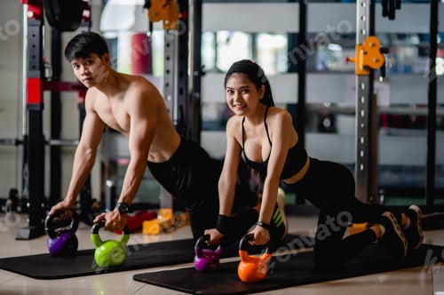 Preview: Young couple doing plank on kettlebell workout at fitness gym