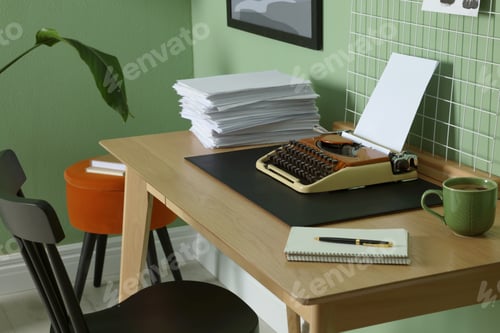 Preview: Typewriter, stack of papers and mood board on wooden table near pale green wall. Writer's workplace
